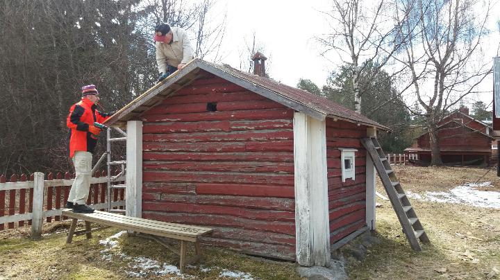 Kaksi miestä korjaa pienen mökin kattoa